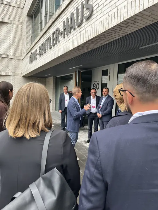 Delegation members gathered at the entrance of the Käthe-Beutler-Haus on Campus Berlin-Buch while a host speaks.