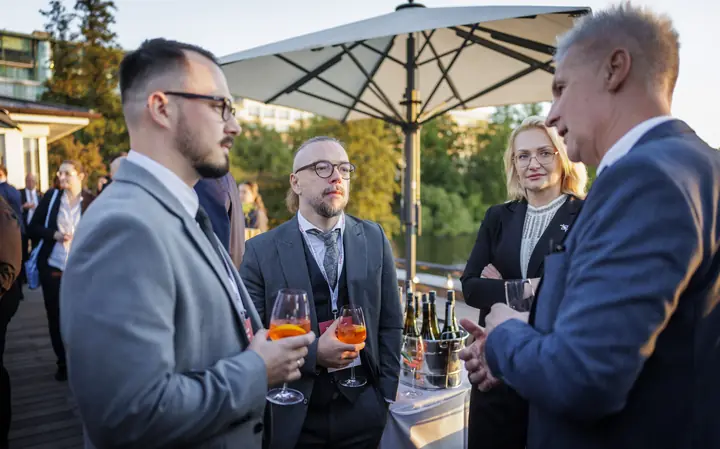 Aleksandrs Gusevs and Armands Baranovskis of Double Helix Technologies in conversation with two other guests at an evening reception on a terrace by the water.