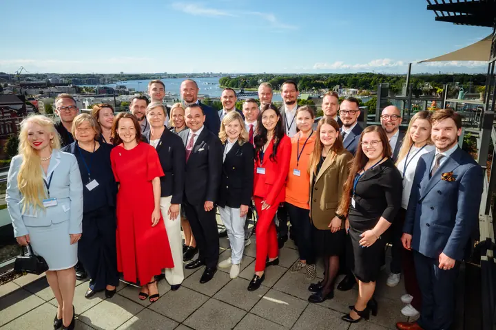 The Latvian partner-country delegation on a rooftop terrace with the Warnow and the port of Rostock behind them.