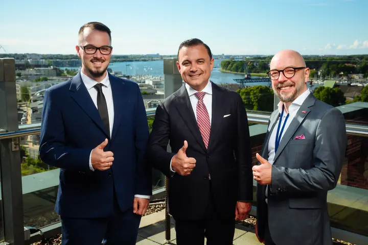 Aleksandrs Gusevs and Armands Baranovskis of Double Helix Technologies with a representative of the Latvian delegation, thumbs up on a rooftop terrace above the Warnow.