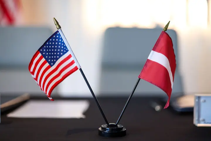 A small US flag and a small Latvian flag side by side on the signing table.