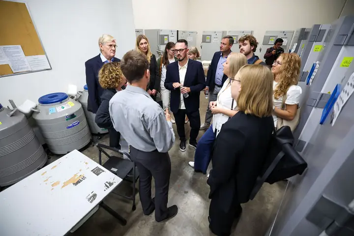 Delegation members in a biobank freezer room, beside liquid nitrogen tanks, listening to their host.
